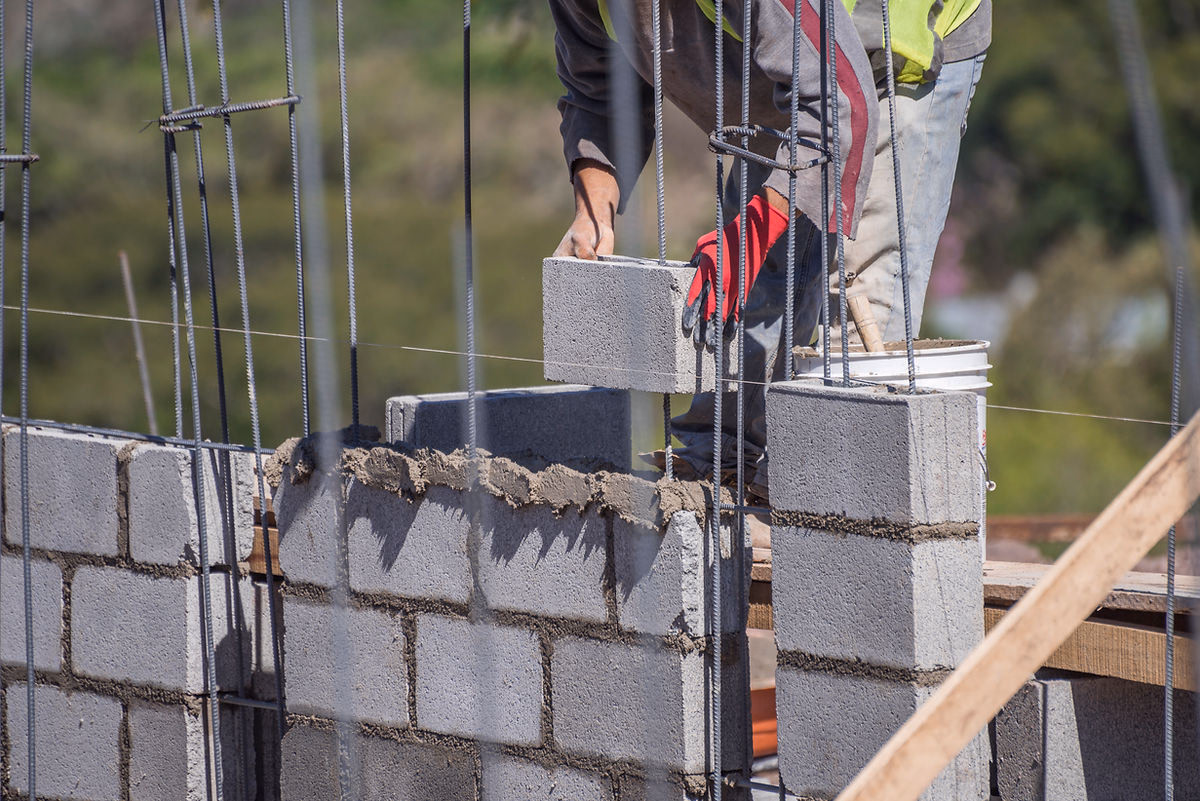 A builder laying concrete blocks with reinforcement bars during a masonry wall build